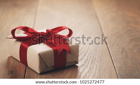 rustic craft paper gift box with red ribbon bow on wood table