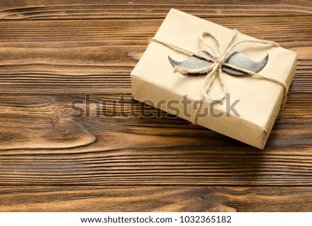 
gift box wrapped in kraft paper with paper mustache on brown wooden background