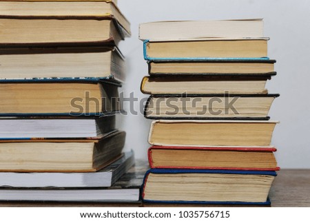 Stack of different books on a table against a white wall background