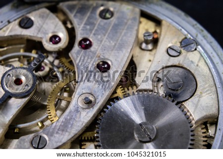 An old watch on a dark table. Timer mechanism seen enlarged. Black background.