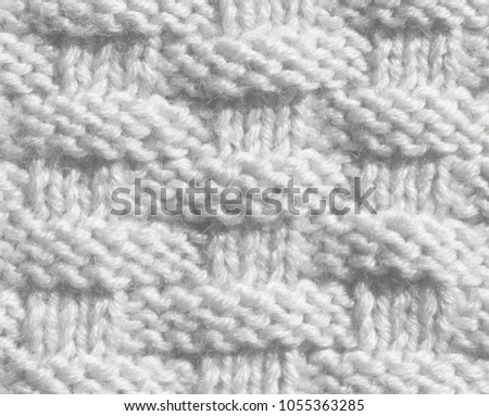 The sample of a knitted cloth of white color. Texture of woolen threads, the product is made by hand.