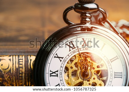 Time running symbol or business deadline concept, closed up vintage pocket watch on book with golden artificial light.