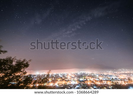 a view from above on a big city at the foot of the mountains, many glowing lights and lanterns under the night sky