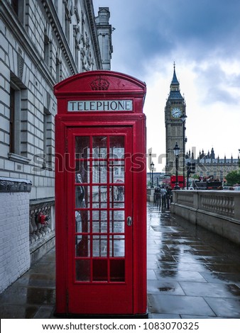 Red telephone booth near London's iconic landmark Big Ben tower on a wet rainy day.
