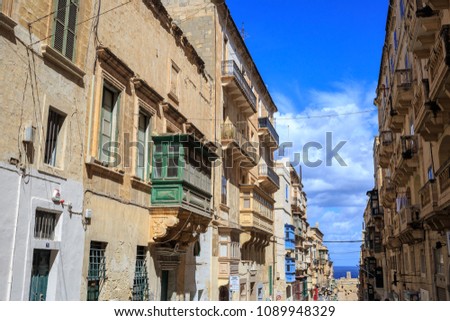 Malta, Valletta, traditional sandstone buildings with colorful wooden windows on covered balconies. Blue sky with clouds and sea background.