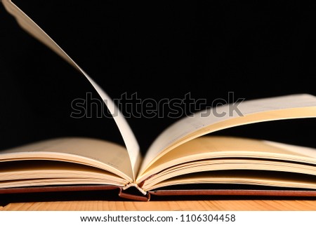 Book was open on wooden table and black background.