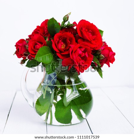 Home roses in a glass vase on a white wooden table.