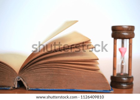 Close-up of old book open on table an hourglass beside selective focus and shallow depth of field