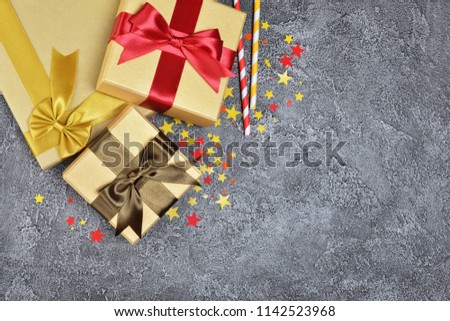 Golden shiny classic gift boxes with color satin bows and paper cocktail straws with confetti in the shape of stars as attributes of party on gray concrete background