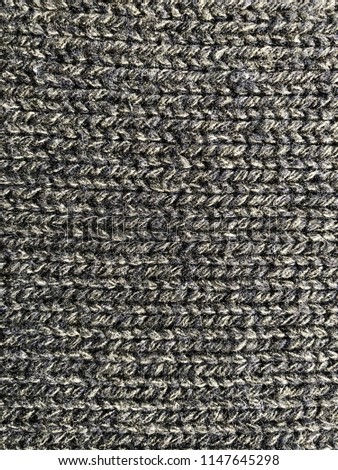 Texture of knitted woolen in dark grey-blue color. Closeup of horizontal knitting loops, fabric seamless texture, background.