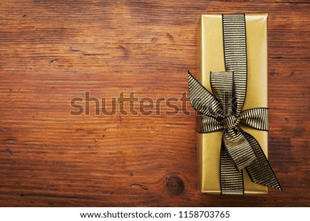 Gift or present box packed in golden paper on wooden table top view. Greeting card for Christmas or birthday.