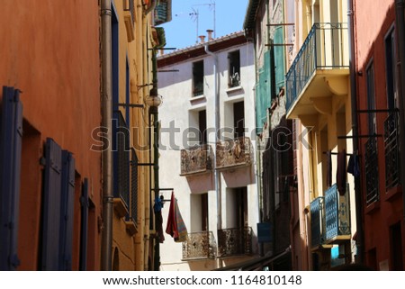 Outdoor view of a typical street of Collioure village, southern France. August, 26, 2018. Colorful facades with wooden doors and windows, and small iron balconies. Sunny day, blue sky in background.