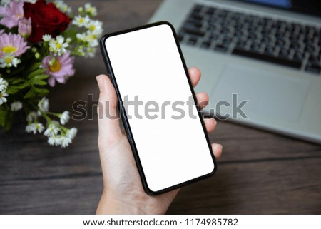 female hand holding phone with isolated screen over desk with laptop and flowers