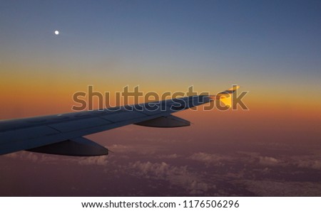 View from airplane window on the wing during sunset over the clouds.