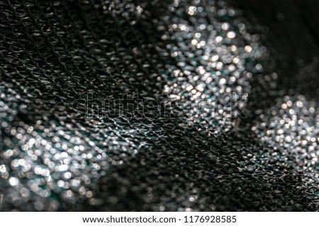 The original texture of the woven network or black nylon net with bokeh and sunlight spots. Black, white, green. Focusing is located on the weave and passes into the soft bokeh. 