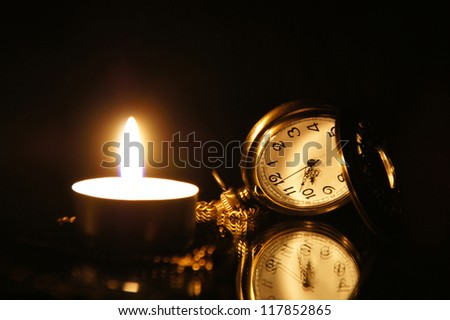 Vintage pocket watch, with burning candle on a the mirror