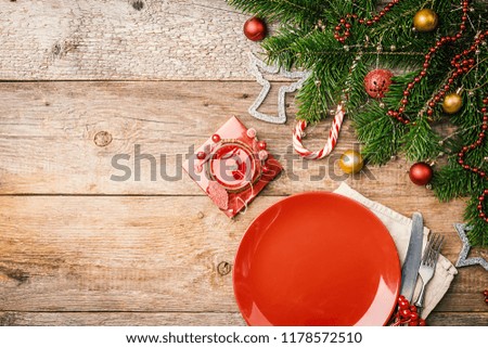 Christmas table place setting with empty red plate and cutlery with festive decorations, fir tree and balls. New Year holiday background, top view