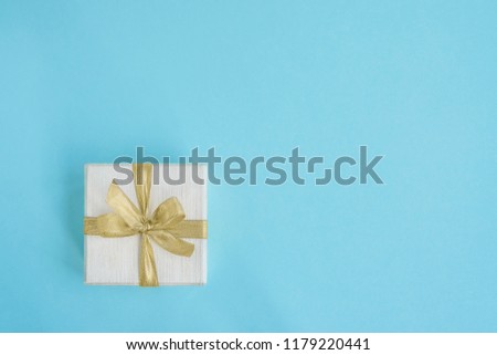 Gift or present box decorated with golden ribbon on light blue background. Top view, copy space. Greeting card. Minimalism.