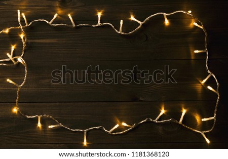 Christmas or New Year fairy lights frame on dark wooden table. Christmas or New year background with copy space
