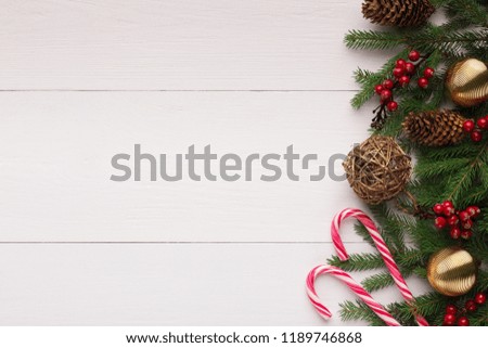 Christmas border. Tree branches with golden baubles, stars, red berries and lollipops on white wooden table, top view, copy space