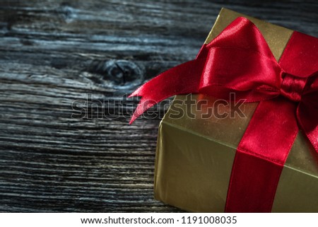 Golden gift box with bow on wooden board.