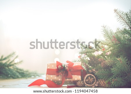Christmas coziness in a room on a light background, with lights and branches of a Christmas tree and a gift with a red bow on the table, space for text