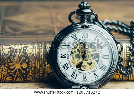Time running, deadline, life time or business milestone concept, closed up vintage pocket watch or clock on book in vintage tone.