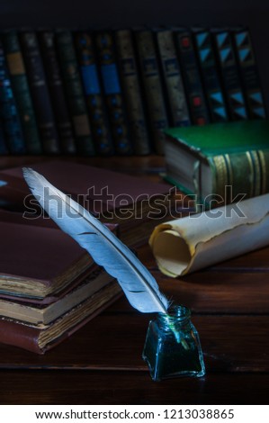 Quill pen and a rolled papyrus sheet on a wooden table with old books