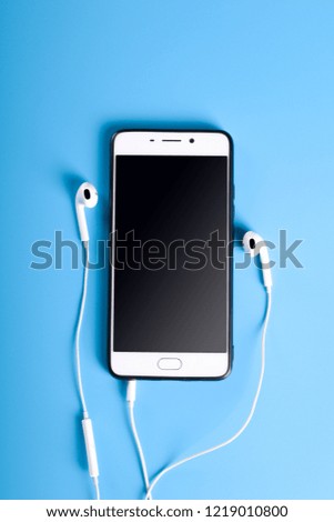 Mobile headphones and a mobile phone of white color on a blue background in light colors with a place for text.
