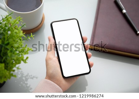 female hand holding touch phone with isolated screen above the table in the office