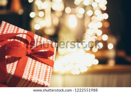 New Year's gift in red and white paper with a red bow on the background of glowing lights