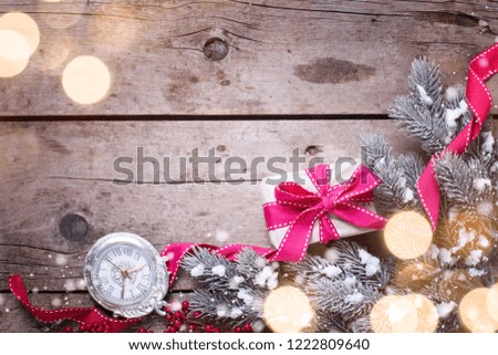 Wrapped christmas gift box, decorative clock and fur tree branches  with bokeh lights on aged wooden background. Selective focus. Place for text.