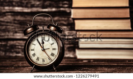 Alarm clock and books on wooden table and background