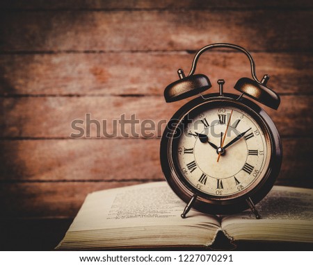 classic alarm clock with bell on a book on wooden table.
