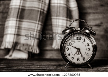 Retro alarm clock and scarf on wooden table. Image in black and white color style
