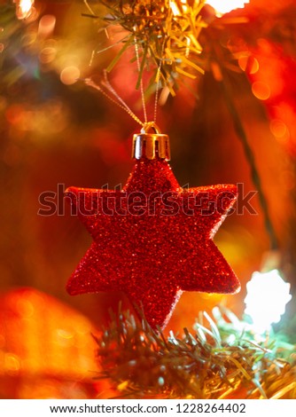 Christmas ornament and decoration. Red glitter star hanging on a christmas tree at home in a warm atmosphere illuminated by artificial lights