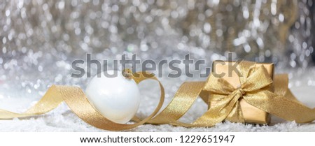 Christmas balls and gift box, golden ribbon and snow, abstract bokeh lights background, banner