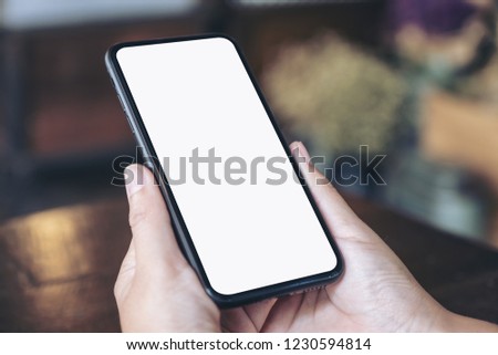 Mockup image of hands holding black mobile phone with blank white screen in vintage cafe