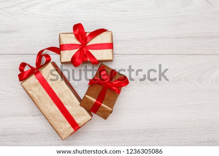 Three gift boxes tied with red ribbons on gray wooden background. Top view with copy space.