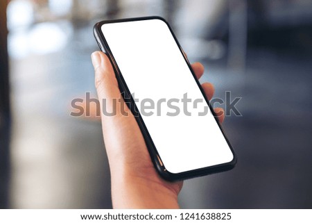 Mockup image of a hand holding black mobile phone with blank white desktop screen