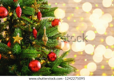 Decorated Christmas tree on soft yellow lights with bokeh effect background. Festive composition with fir and blurry sparkling backdrop, new year holiday decorations. Close up, copy space.
