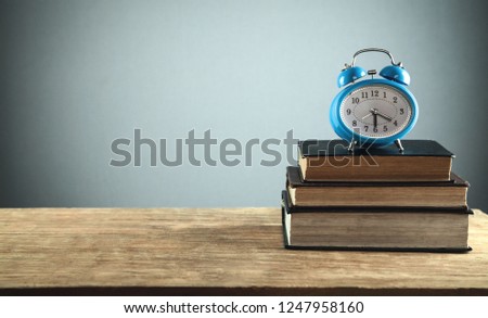 Blue alarm clock and books on wooden table.