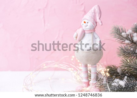 Little decorative snowman  toy, fir tree branches and fairy lights on bright  pink wooden  background. Winter holidays, Christmas, New Year concept. Place for text. Selective focus.