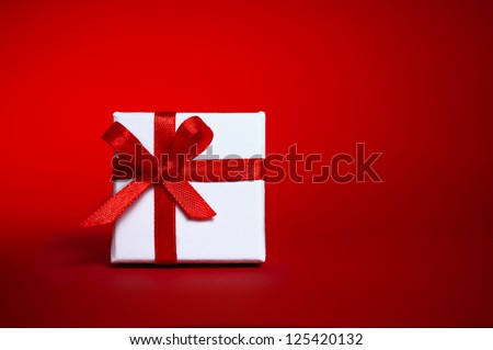 White gift box with red ribbon bow on red background