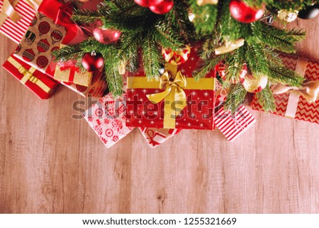 Top view composition of Christmas tree branches with stack of different presents in colorful festive wrapping tied with bow. Pile of gifts under spruce tree on wooden floor. Background, copy space.