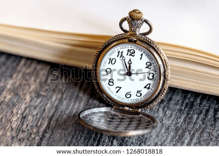 Vintage pocket watch with open book on the dark wood table
