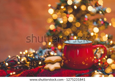 Red mug of hot coffe with Christmas lights, fresh cookies and Christmas tree 