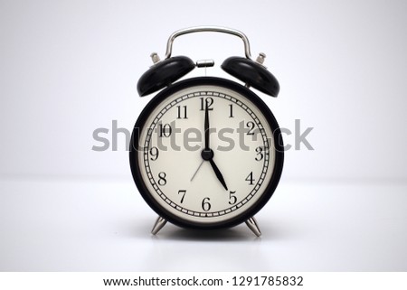 Black vintage alarm clock on table. White background. Wake up concept. An image of a retro clock showing 05:00 pm/am.                                