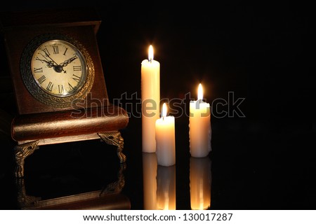 Vintage wooden clock near lighting candles on dark background