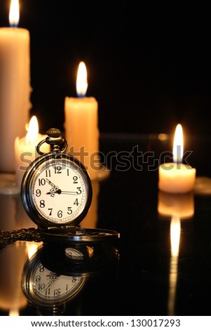 Pocket watch near lighting candles on dark background